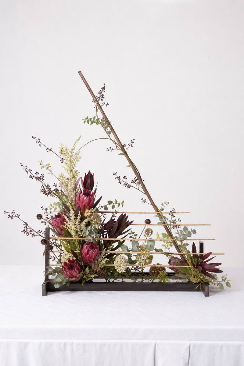 Portrait-format example of a contemporary Between the lines arrangement with a frame, proteas and visible horizontal and diagonal lines.