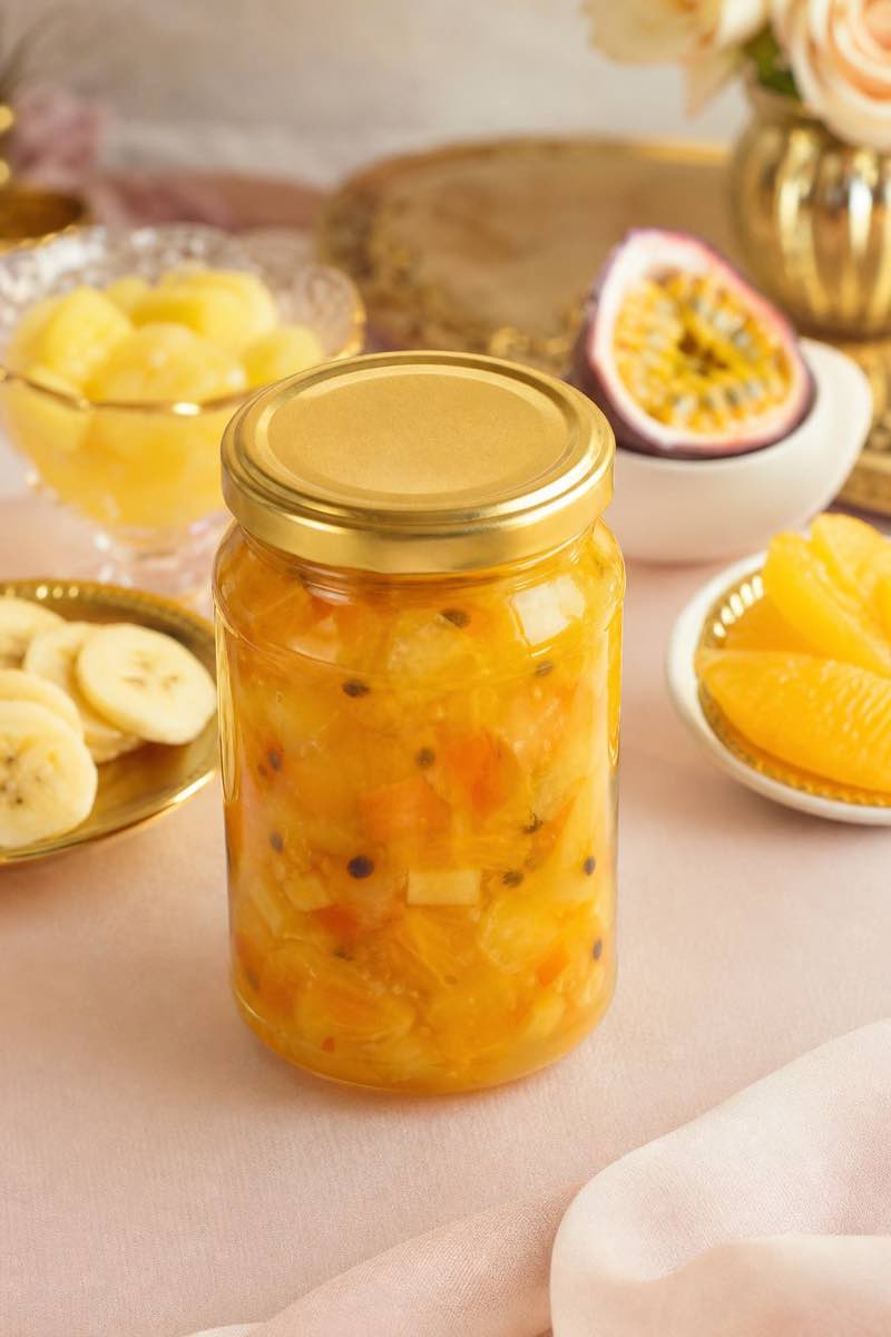Portrait-format example of golden fruit-salad jam with banana, pineapple and granadilla in a honey jar.